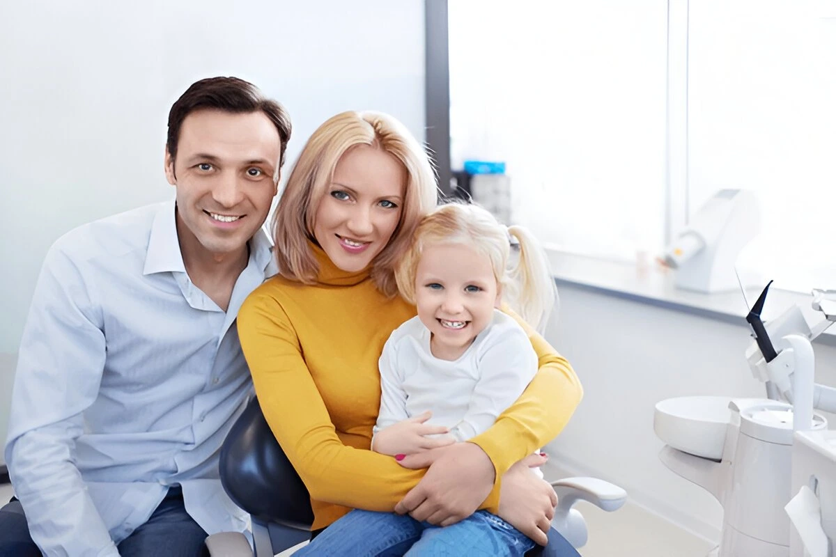 Parents and young daughter smiling together in a dental office
